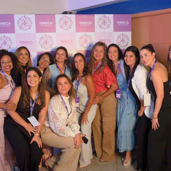 Grupo de enfermeiras participantes do Gineca Weekend posando juntas em frente ao painel do evento.