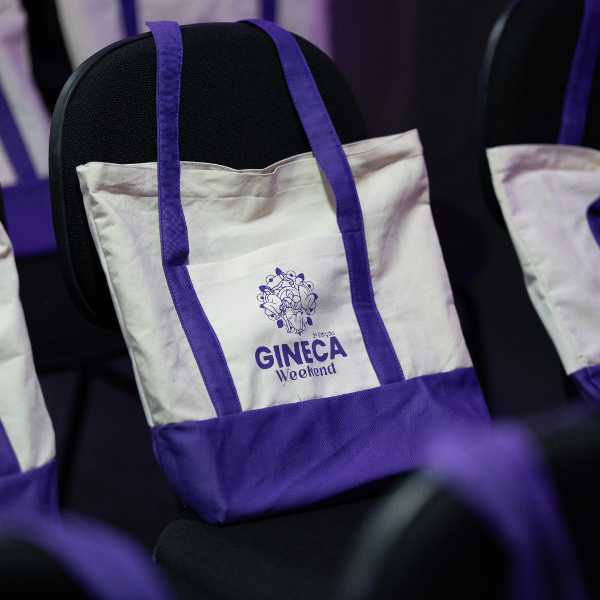 Sacolas oficiais roxas do Gineca Weekend organizadas nas cadeiras do auditório.
